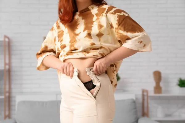 Image of woman trying to do her trousers up after pregnancy weight gain Alton