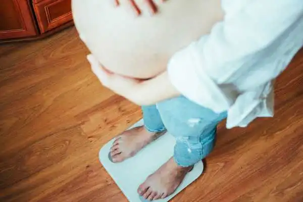 Image of woman weighing herself and experiencing weight gain through pregnancy Alton